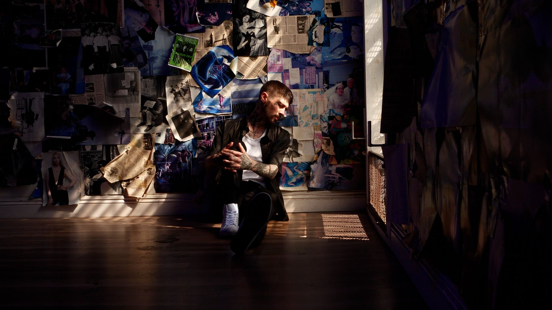 Liam Horne seated in a dark room with a collage wall